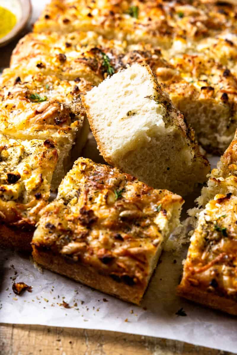 three-quarters view of no knead focaccia cut into squares with one upturned to show the texture.