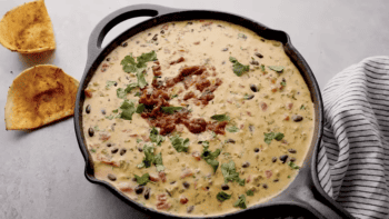 A flavorful Mexican black bean dip with melted Velveeta cheese and a touch of Rotel, served sizzling hot in a skillet alongside crispy tortilla chips.
