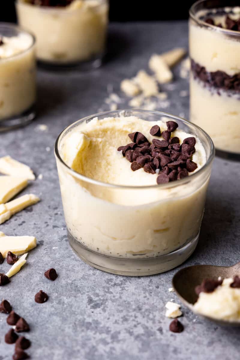 distant three-quarters view of white chocolate mousse in a small glass cup with a bite missing and chocolate chips on top.