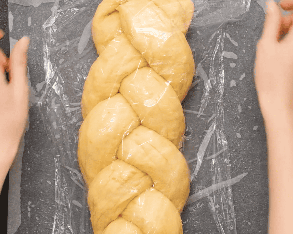 Covering the braided dough with plastic wrap so it can rise.