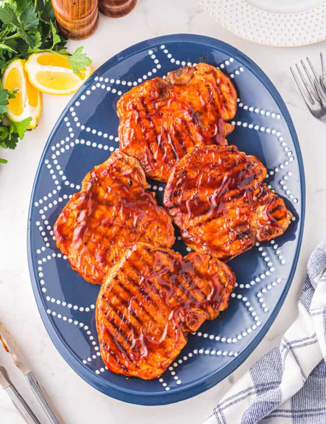 overhead view of 4 bbq pork chops on a blue plate.