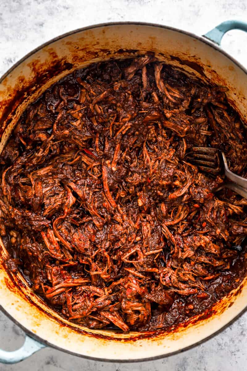 overhead view of shredded birria taco meat in a blue and white dutch oven.