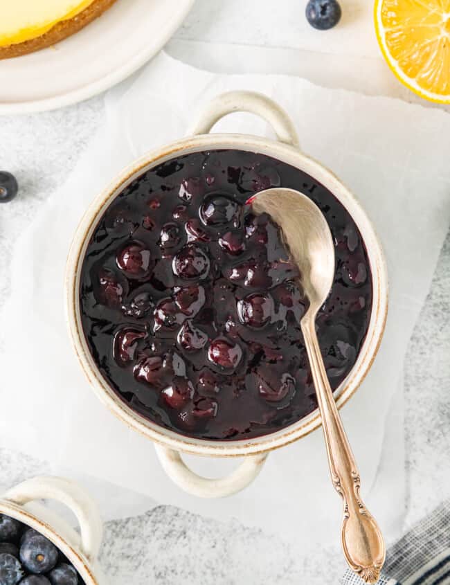 overhead view of blueberry compote in a small white cocotte with a spoon.