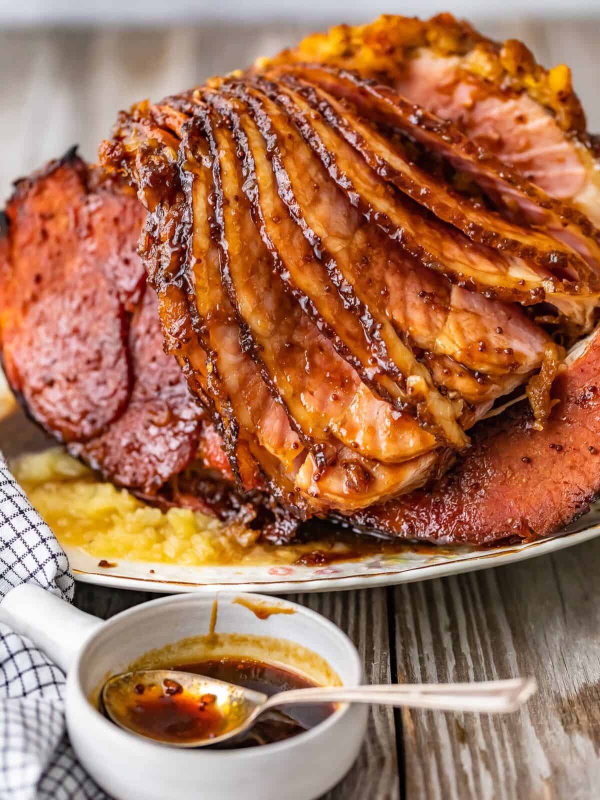 pineapple ham on a serving platter, next to a small bowl of brown sugar glaze