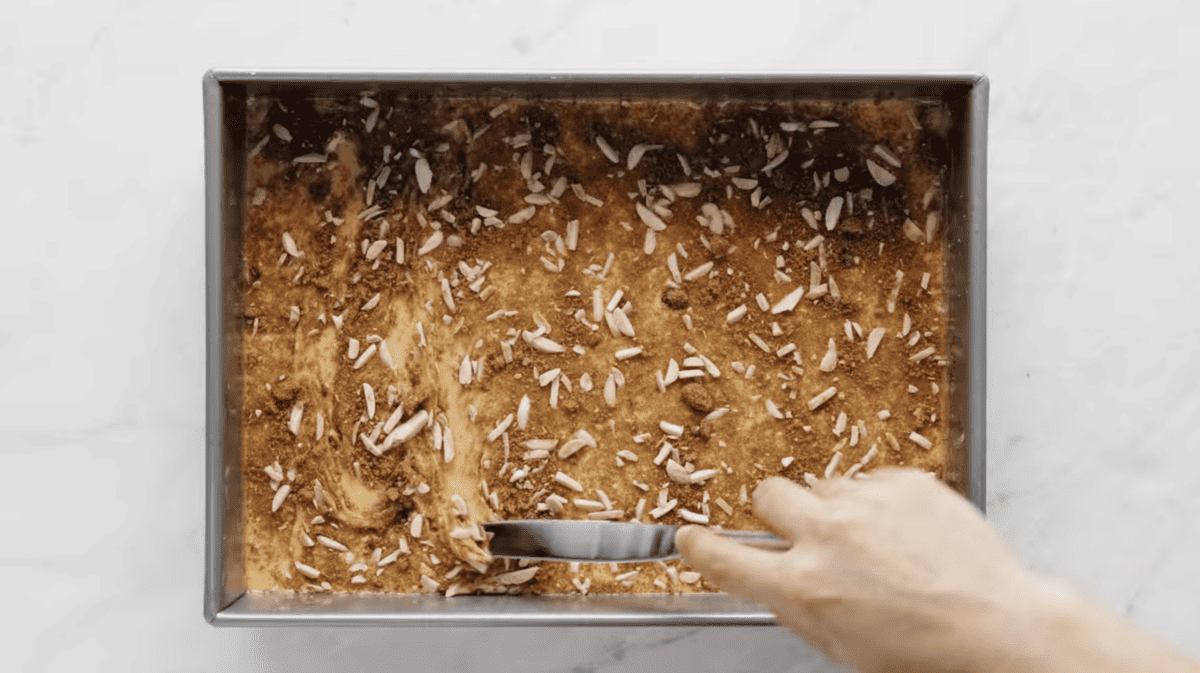 a knife swirling streusel into cake batter in a baking pan.