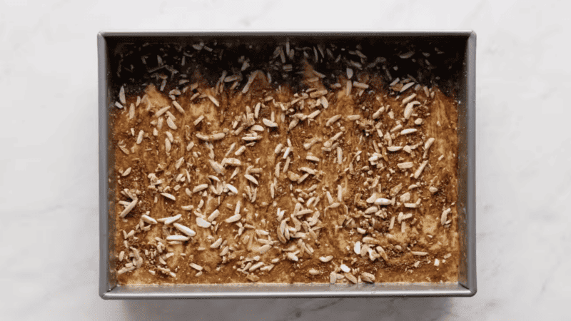 A coffee cake in a metal pan with nuts on top.