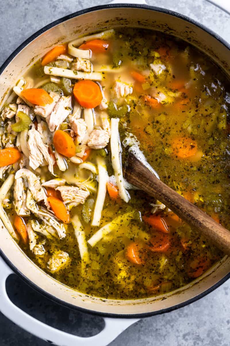 overhead view of homemade chicken noodle soup in a white dutch oven with a wooden spoon.