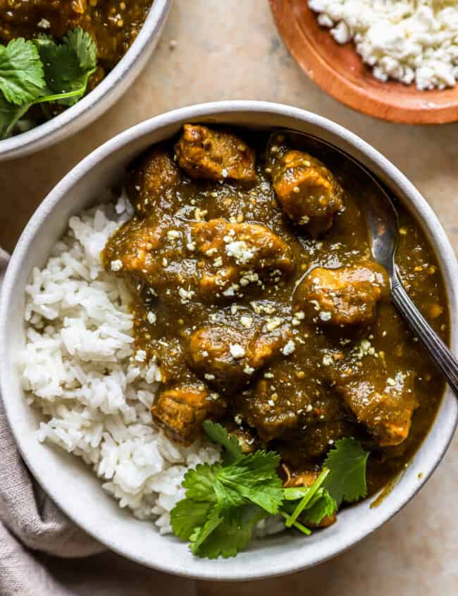 overhead view of a serving of chile verde in a white bowl with white rice, cilantro, and a fork.