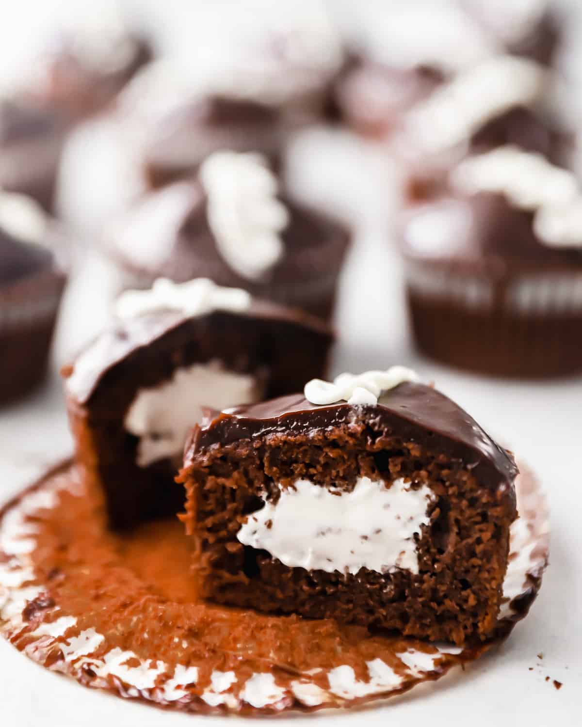 side view of a halved chocolate hostess cupcake showing the filling on top of a cupcake liner.
