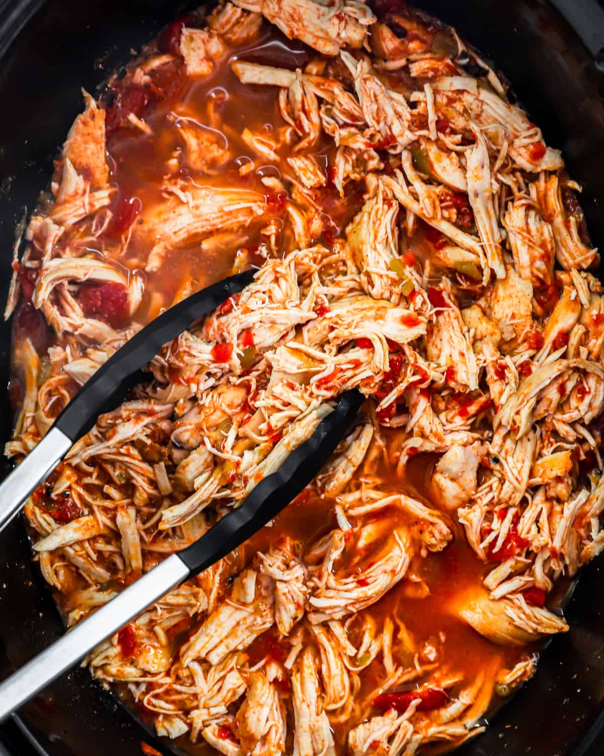 overhead view of shredded crockpot chicken taco meat in a slow cooker with tongs.