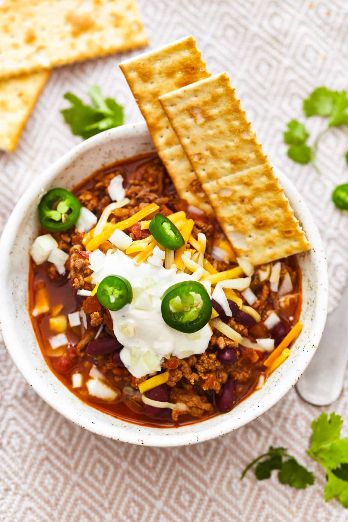 overhead view of a bowl of easy homemade chili with toppings and crackers