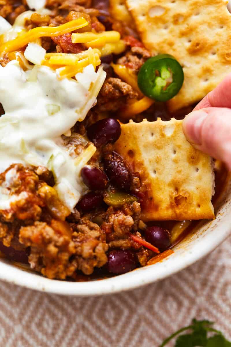 hand dipping a cracker into a bowl of homemade chili