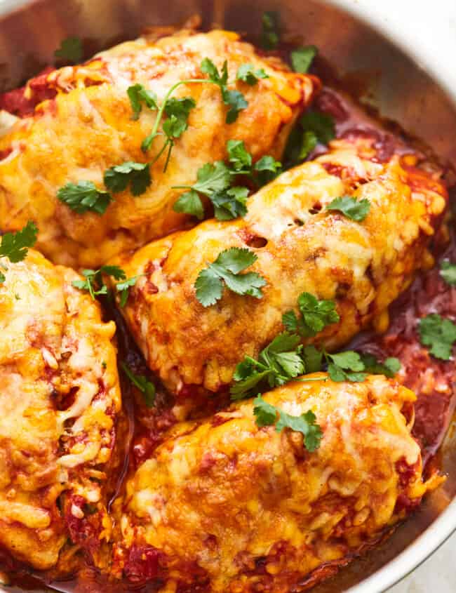 overhead view of 4 enchilada stuffed chicken breasts in a frying pan.