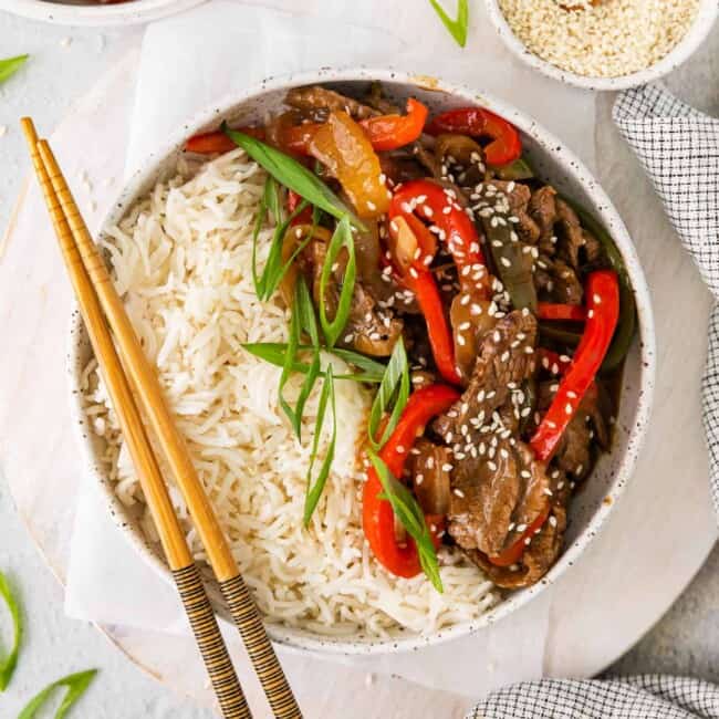 a bowl of beef and pepper stir fry with rice and chopsticks.
