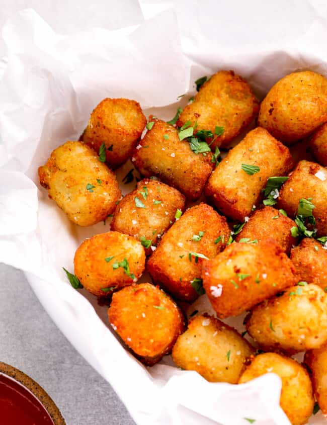 three-quarters view of tater tots in a parchment-lined serving dish topped with parsley.