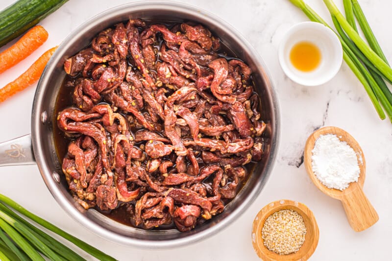 a pan with beef, carrots, onions, and sesame seeds.