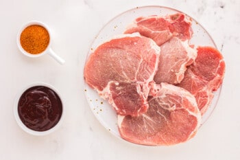 overhead view of 4 raw pork chops on a white plate.