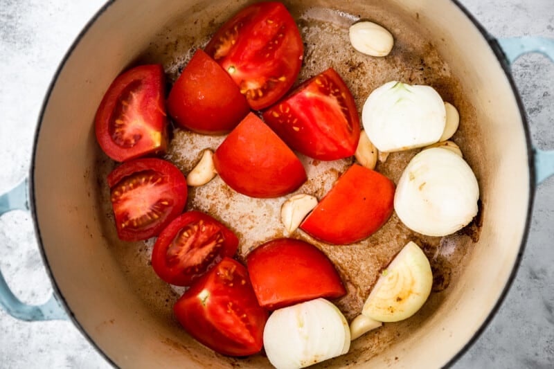 tomato, garlic, and onion in a blue and white dutch oven.