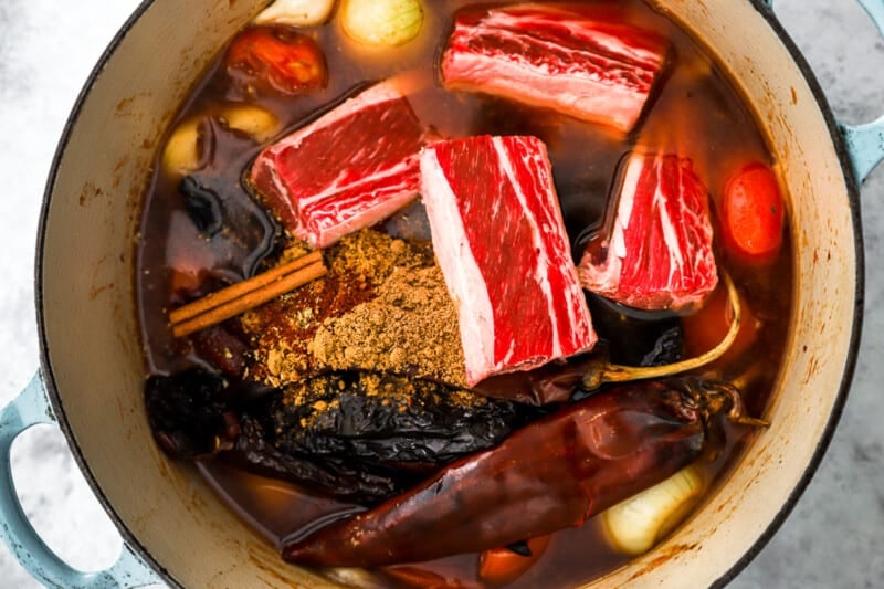 short ribs added to birria in a blue and white dutch oven.