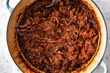 shredded birria taco meat in a blue and white dutch oven.