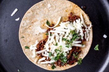 a flattened tortilla with birria taco meat and cheese on half of it.
