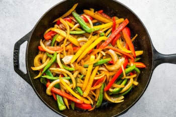 sliced peppers and onions in a cast iron skillet.