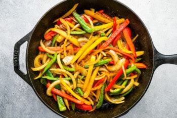 sliced peppers and onions in a cast iron skillet.