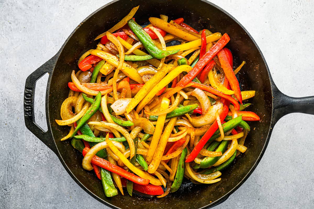 Sliced peppers and onions in a cast iron skillet.