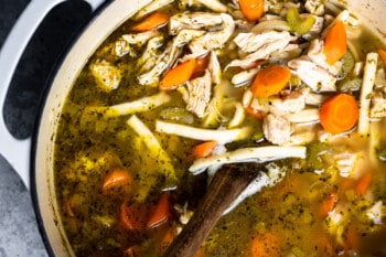 overhead view of homemade chicken noodle soup in a dutch oven with egg noodles and a wooden spoon.