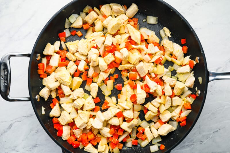chicken, peppers, and onions in a frying pan.