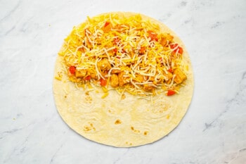 chicken mixture sandwiched between two layers of cheese on one half of a flat flour tortilla.