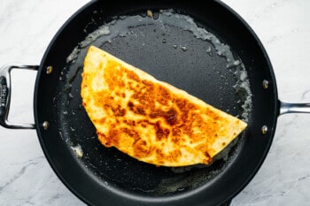 a cooked folded chicken quesadilla in a frying pan.