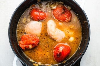 bay leaves, chicken broth, and chicken breasts added to tomatoes, onion, and garlic in a dutch oven.
