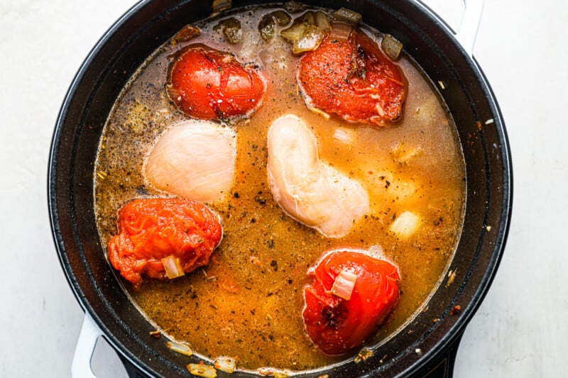 bay leaves, chicken broth, and chicken breasts added to tomatoes, onion, and garlic in a dutch oven.