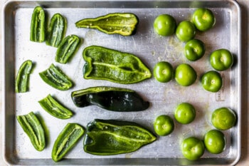 tomatillos and halved peppers on a baking sheet.