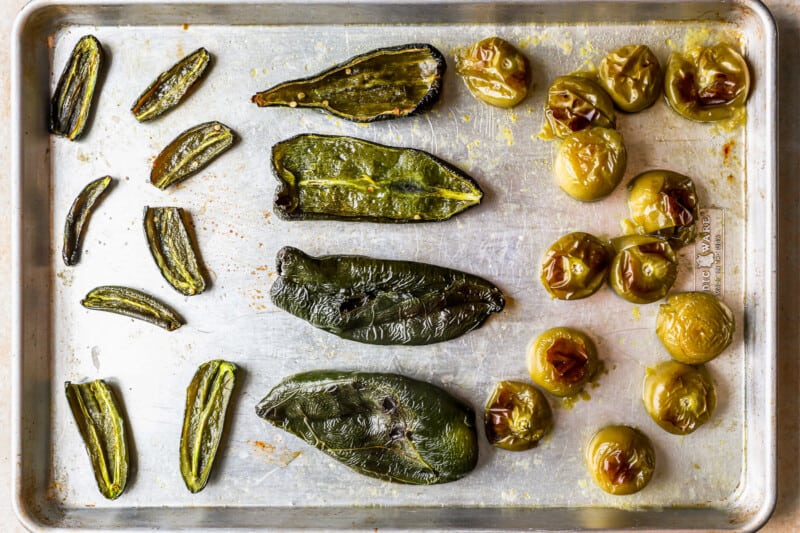 roasted tomatillos and halved peppers on a baking sheet.