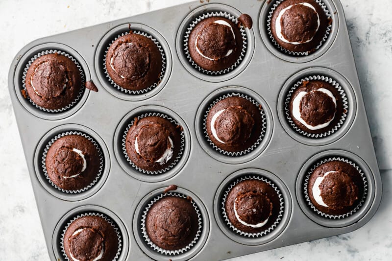 overhead view of 12 cream-filled chocolate cupcakes in a cupcake tin with the tops pushed back on.