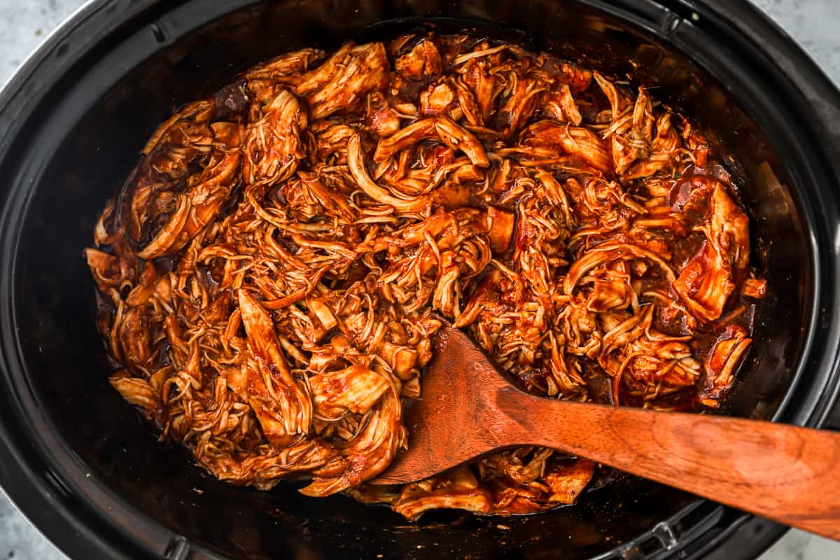 bbq pulled pork in a slow cooker with a wooden spoon.