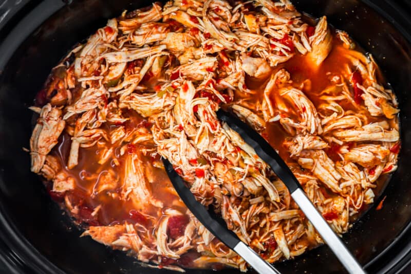 shredded crockpot chicken taco meat in a crockpot with tongs.