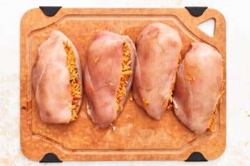4 raw enchilada stuffed chicken breasts on a cutting board.