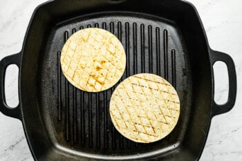 2 grilled corn tortillas in a square cast iron grill pan.