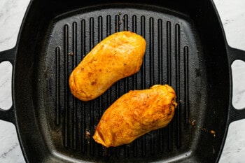 2 grilled chicken breasts in a square cast iron grill pan.