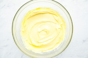 oil added to whipped egg yolks, mustard, and vinegar in a glass bowl.