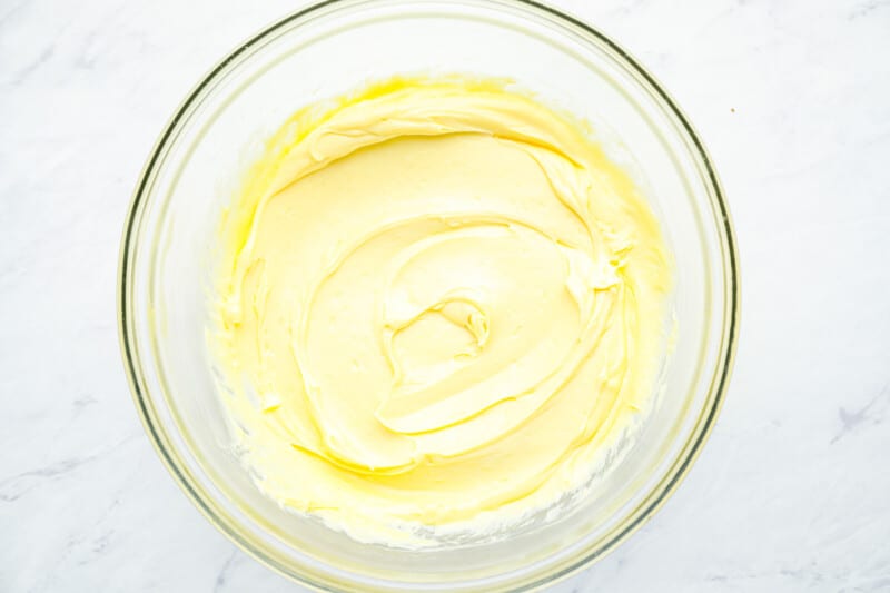 oil added to whipped egg yolks, mustard, and vinegar in a glass bowl.