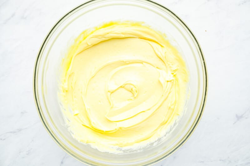 oil added to whipped egg yolks, mustard, and vinegar in a glass bowl.