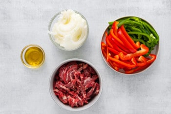 three bowls of meat, peppers and onions on a grey background.