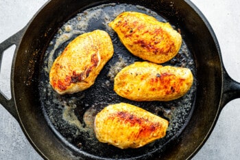 4 cooked seasoned chicken breasts in a cast iron pan.
