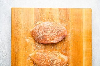 2 raw seasoned chicken breasts on a cutting board.