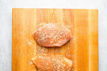 2 raw seasoned chicken breasts on a cutting board.