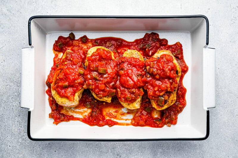 4 cooked chicken breasts covered in salsa in a white rectangular baking pan.